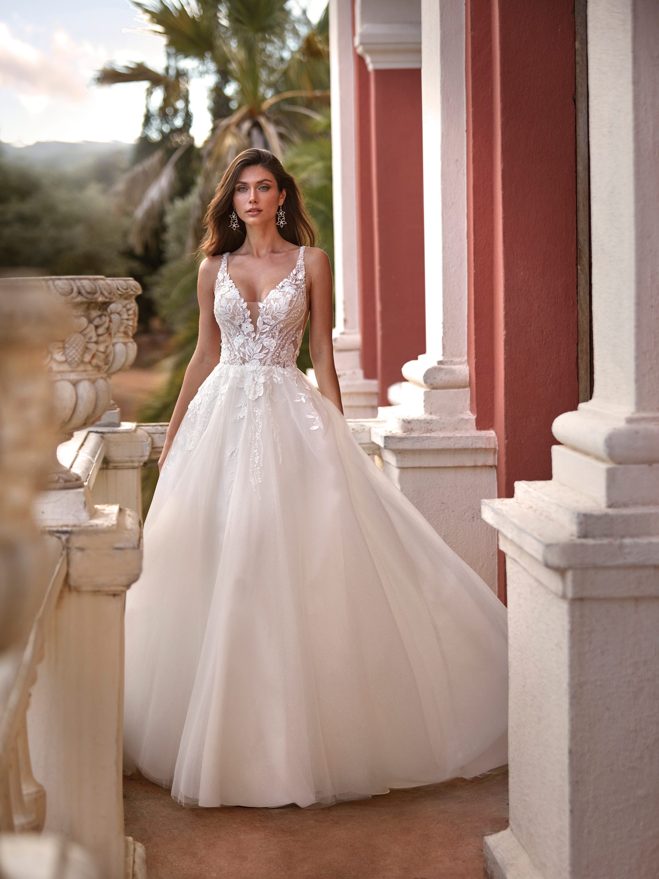 Frau in weißem A-Linien-Brautkleid mit Spitze vor Säulen und Palmen.