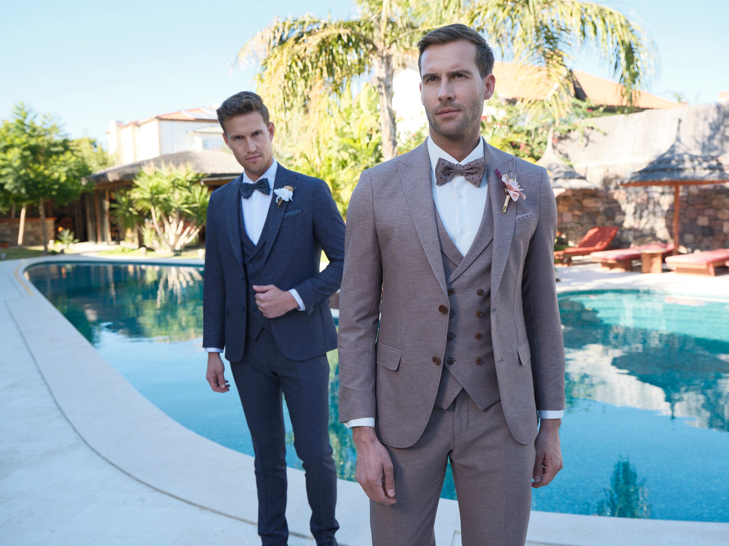 Zwei Männer tragen elegante Anzüge mit Fliegen am Pool in sonniger Gartenanlage.