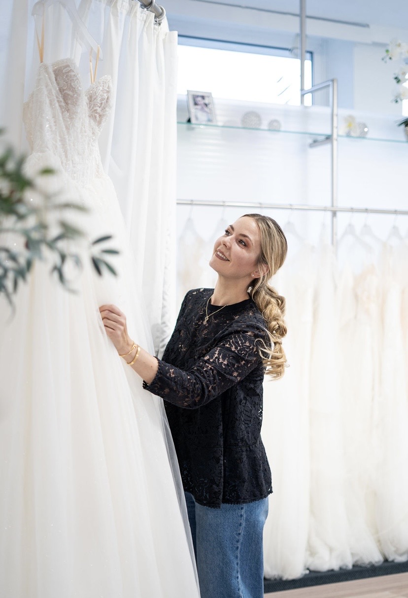 Fünf Frauen stoßen mit Sektgläsern an, eine trägt ein weißes Hochzeitskleid in einem Brautmodengeschäft.